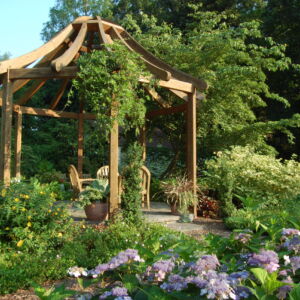 Arthur Rudolph was a beloved sales representative from Monrovia Nursery. This garden, named for him, features the Lillian Koelsch gazebo, a patio, and a bubbling urn water feature. It also highlights plants that will provide color and interest in a part-sun and part-shade setting, as is typical of many home gardens. Gardeners can gain inspiration from the many lovely monocots and native perennials.<br/><br/><a href="/gardens/art-rudolph-sun-and-shade-garden/">Art Rudolph Sun and Shade Garden</a> gazebo in garden with purple and yellow flowers